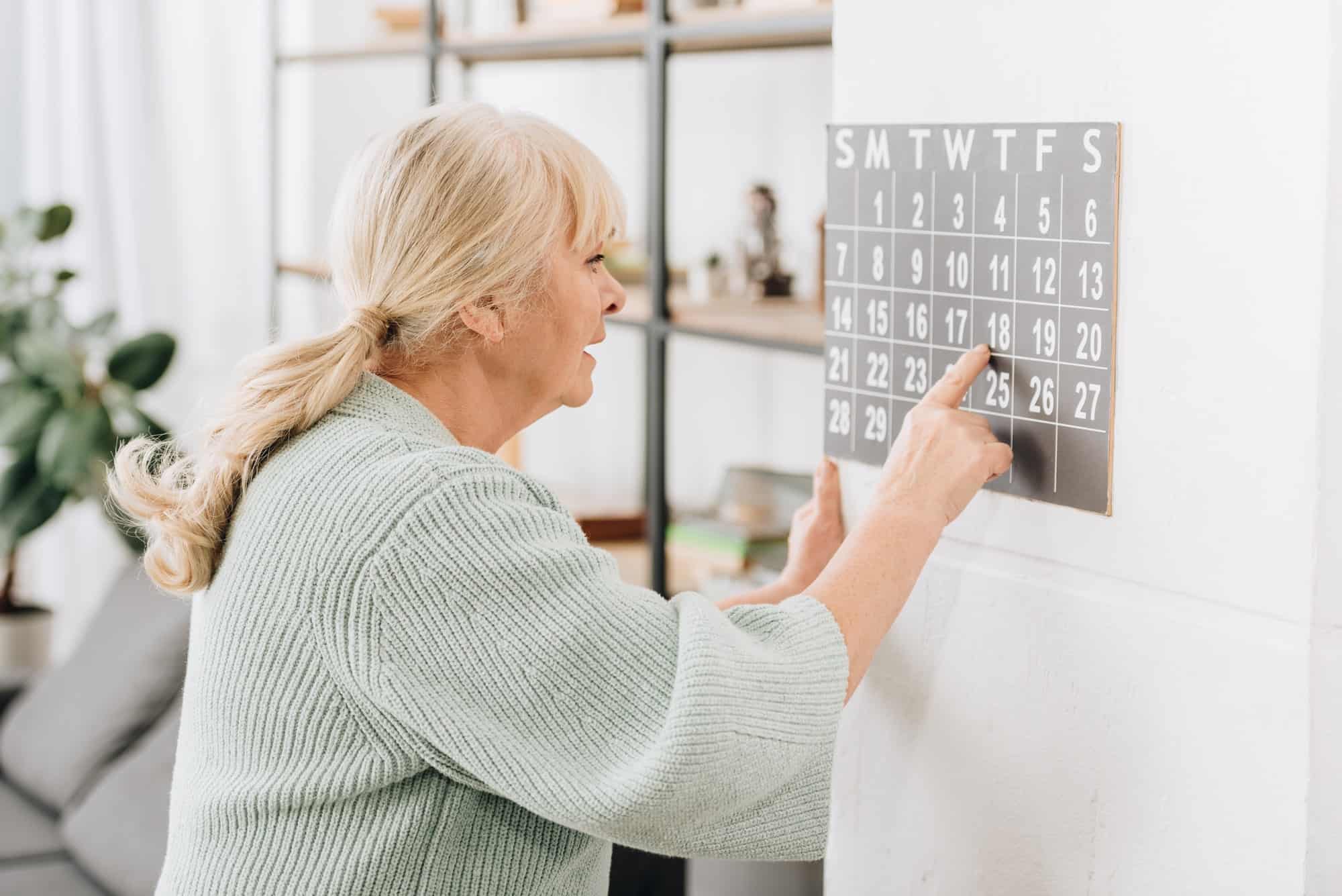 senior woman touching wall calendar and looking at dates