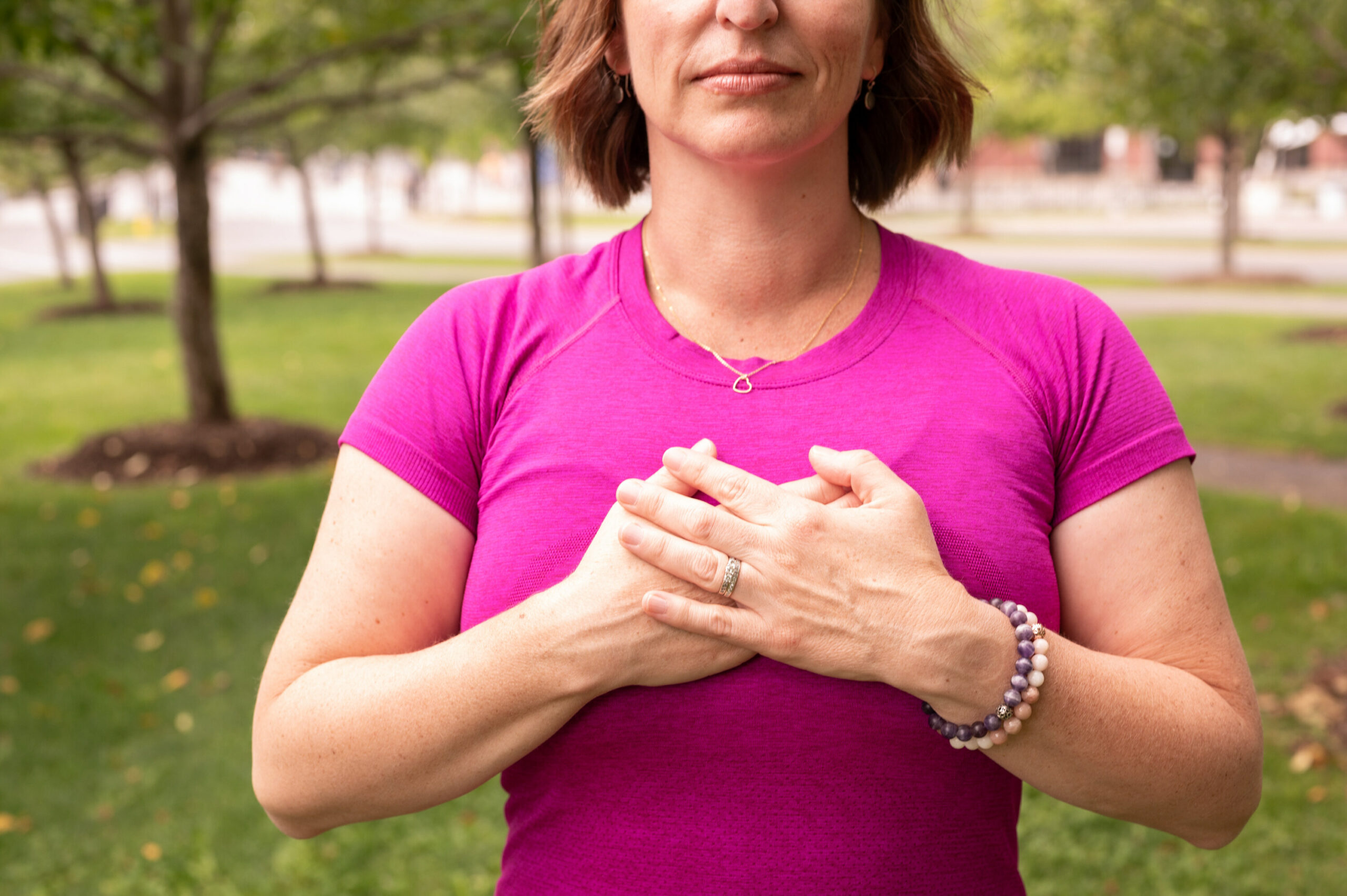 Cancer physiotherapist Beth Hoag is standing with her hands over her chest wearing a bright pink shirt.