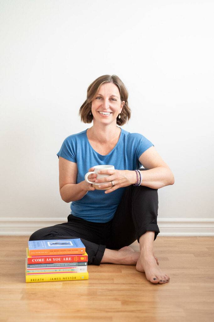 Beth Hoag sits with a stack of books on cancer, physiotherapy, cancer rehab and the importance of movement.