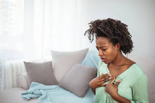 Woman in green shirt sitting on her couch experiencing symptoms from Radiation Fibrosis Syndrome.