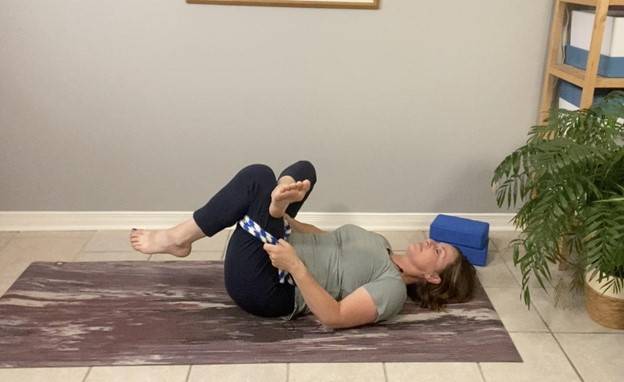 Beth Hoag, Physiotherapist, laying on her back on the floor with a band behind her thigh pulling her bent leg toward her, a beneficial glute stretch after pelvic radiation therapy.