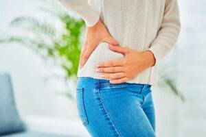 Woman holding on to her hip, low back area, experiencing pain as a side effect from pelvic radiation therapy.