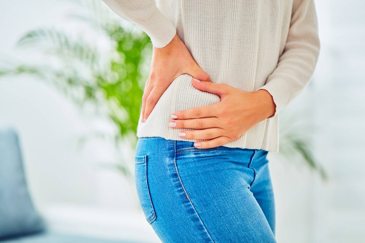 Woman holding on to her hip, low back area, experiencing pain as a side effect from pelvic radiation therapy.