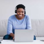 Black woman sitting on couch, having video chat on laptop