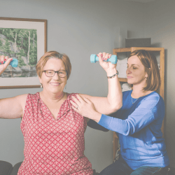Beth Hoag is working with a cancer rehabilitation client, helping her align her shoulder while lifting small weights.