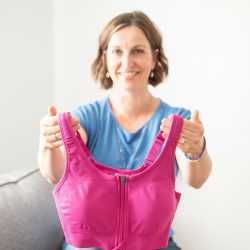 Beth Hoag holding a bright pink compression bra used for breast cancer rehabilitation.